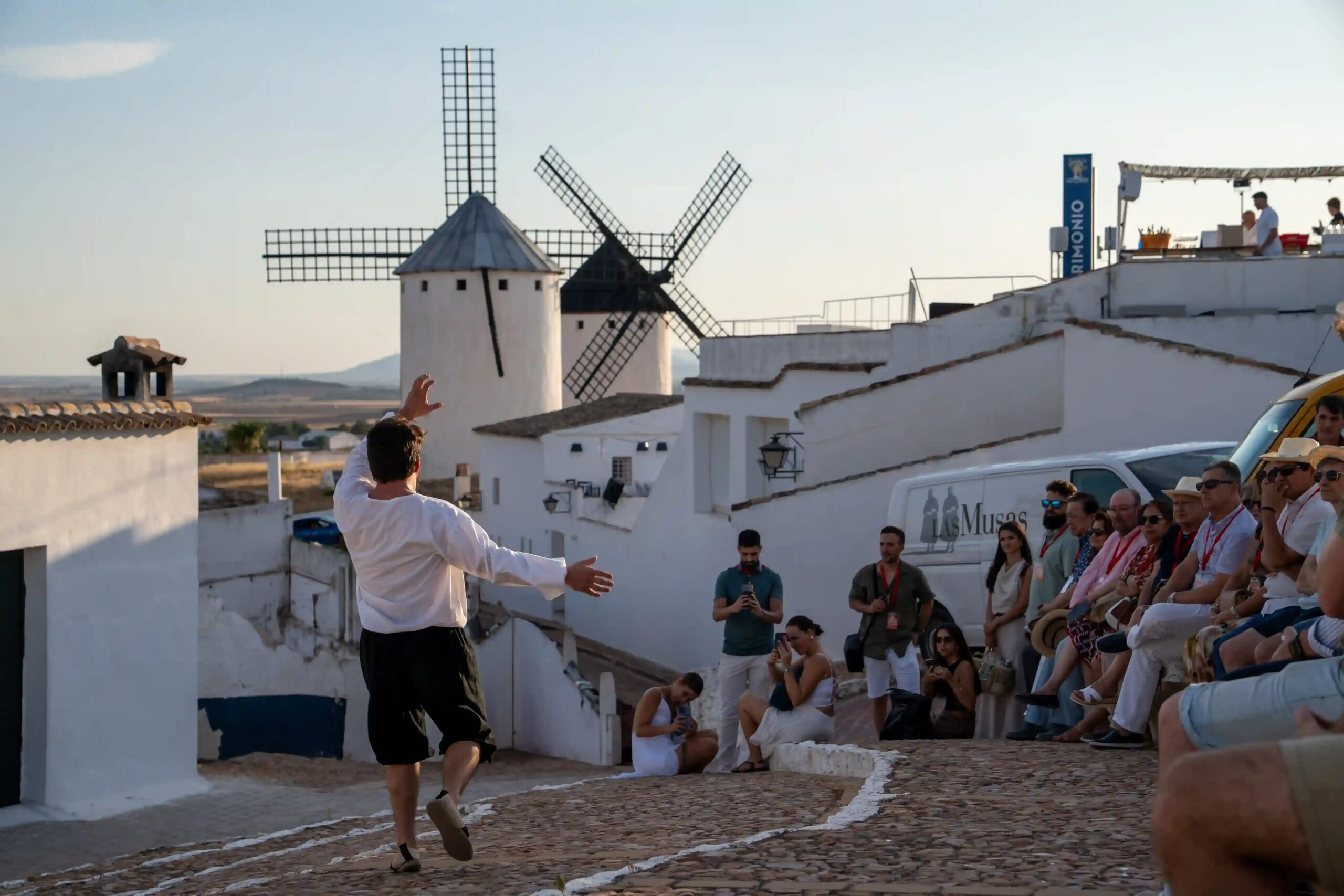 Persona actuando en una calle de pueblo con molinos de fondo en el evento de Sabor Quijote en Campo de Criptana